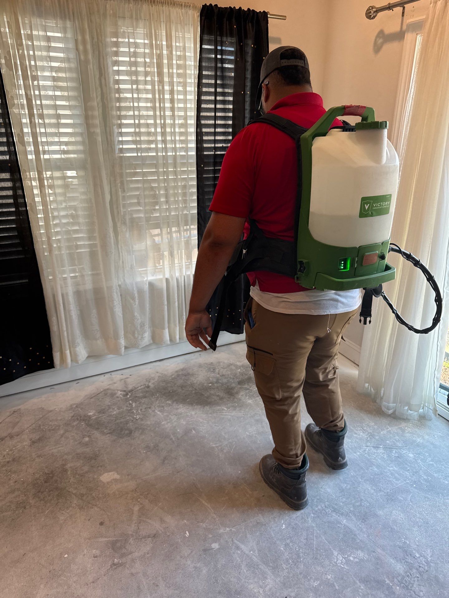 Technician Performing Mold Remediation Using An Antimicrobial Sprayer In A Residential Room With Exposed Subfloor Following Water Damage.