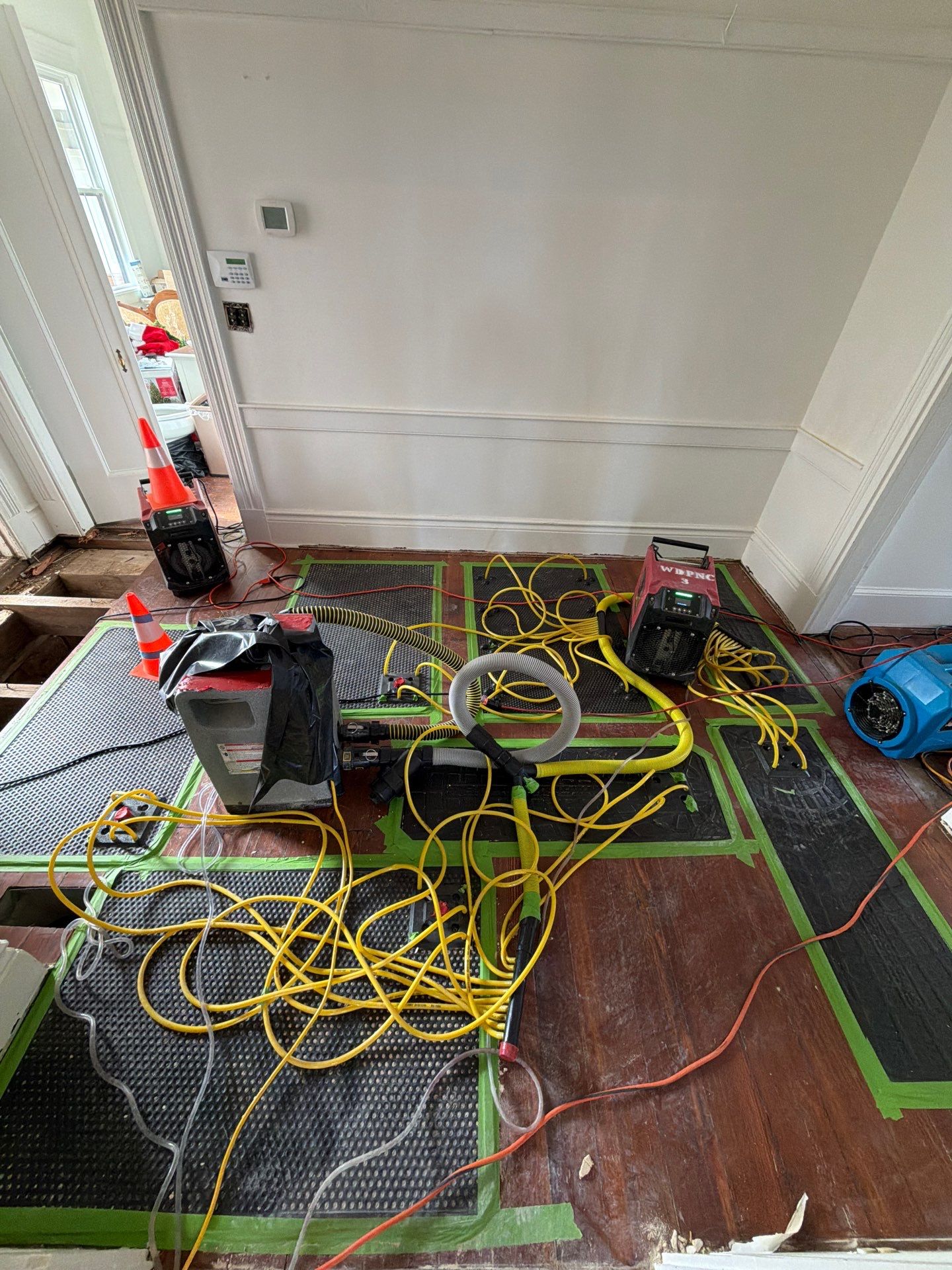 How Do You Dry Drywall Safely After A Leak In Fayetteville Homes? 12 Water Damage Restoration Floor Drying System With Drying Mats And Hoses Sealed To Hardwood Flooring, With Dehumidifiers And Air Movers For Structural Drying.