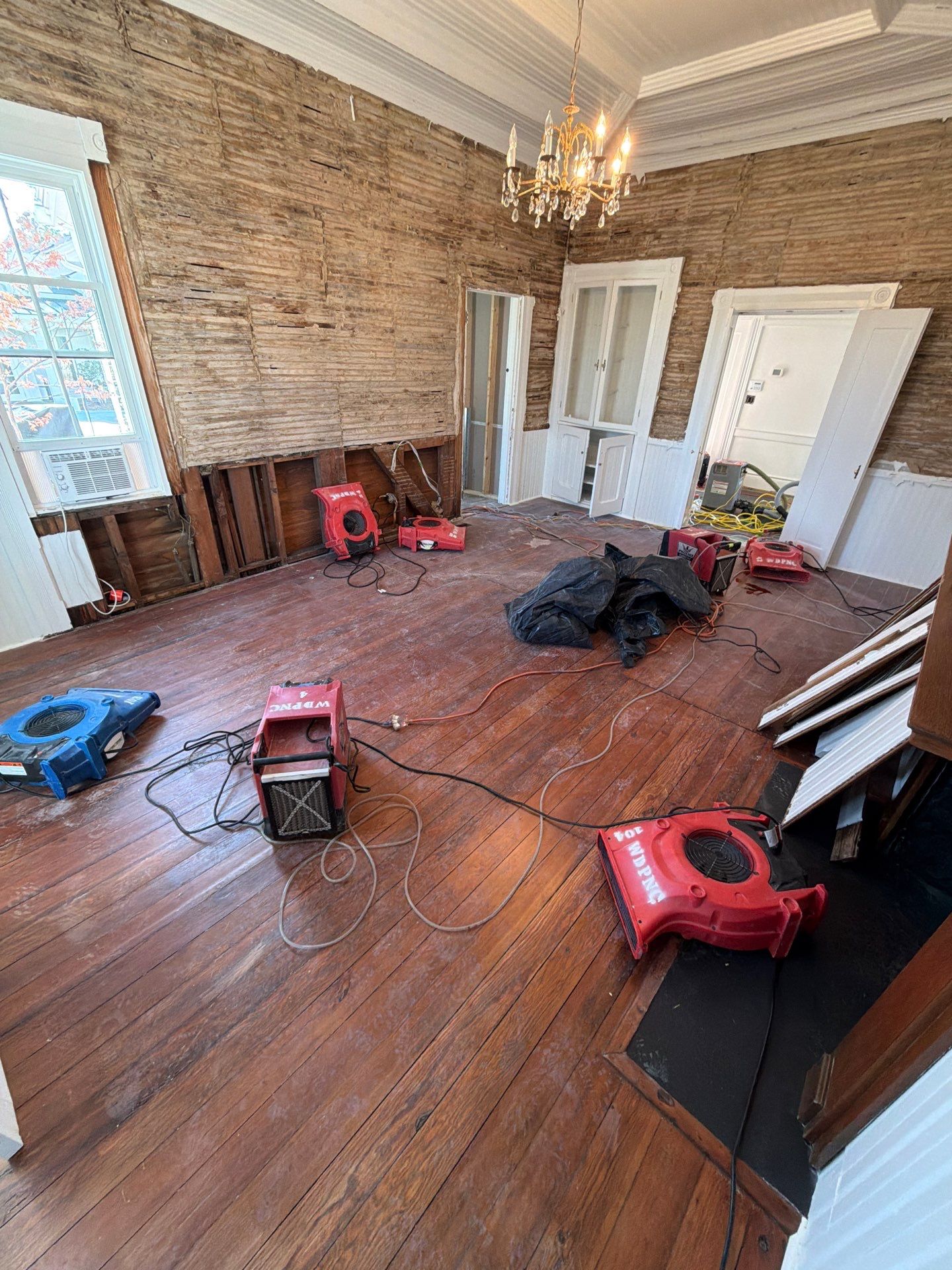 How Do Professionals Detect Moisture Behind Walls? 14 Water Damage Restoration Drying Setup In A Residential Room, With Air Movers And A Dehumidifier, Wall Baseboards Removed For Moisture Mitigation.