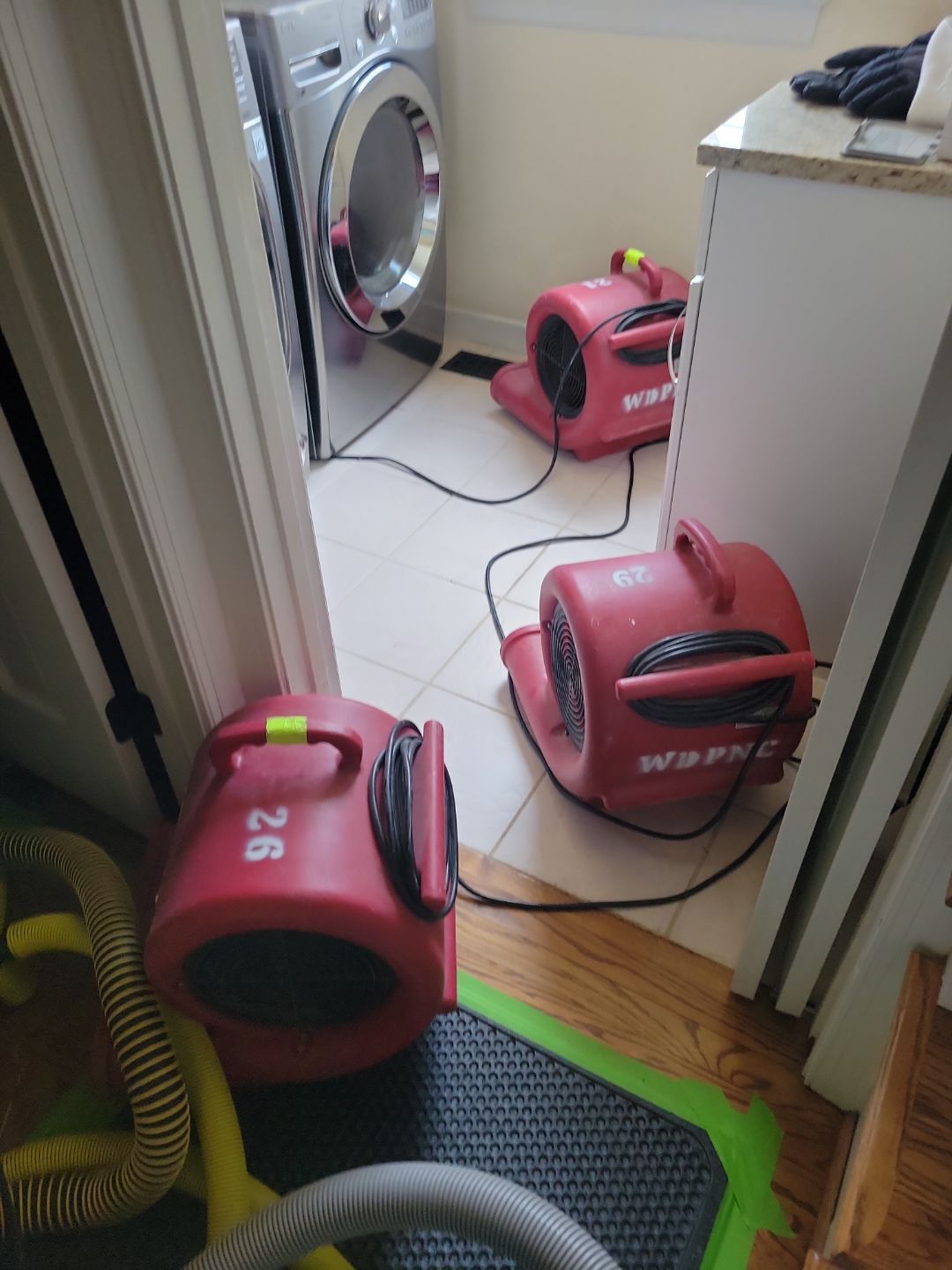 What Causes Recurring Musty Smells After Water Damage In Burlington? 13 Water Damage Drying Equipment In A Laundry Room, With Multiple Air Movers Positioned To Dry Tile Flooring And Surrounding Areas Near The Washer And Dryer.